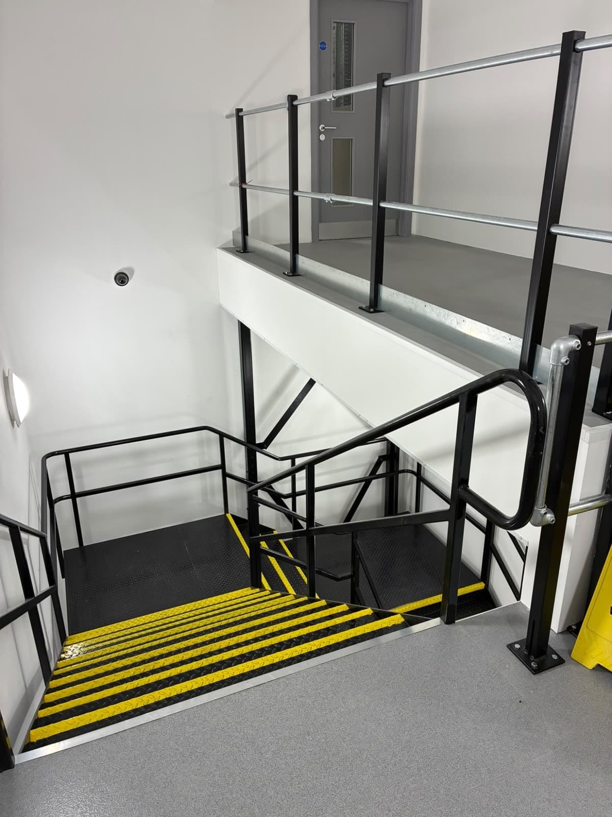 Stairwell with white walls, black railings and a grey door on the landing above