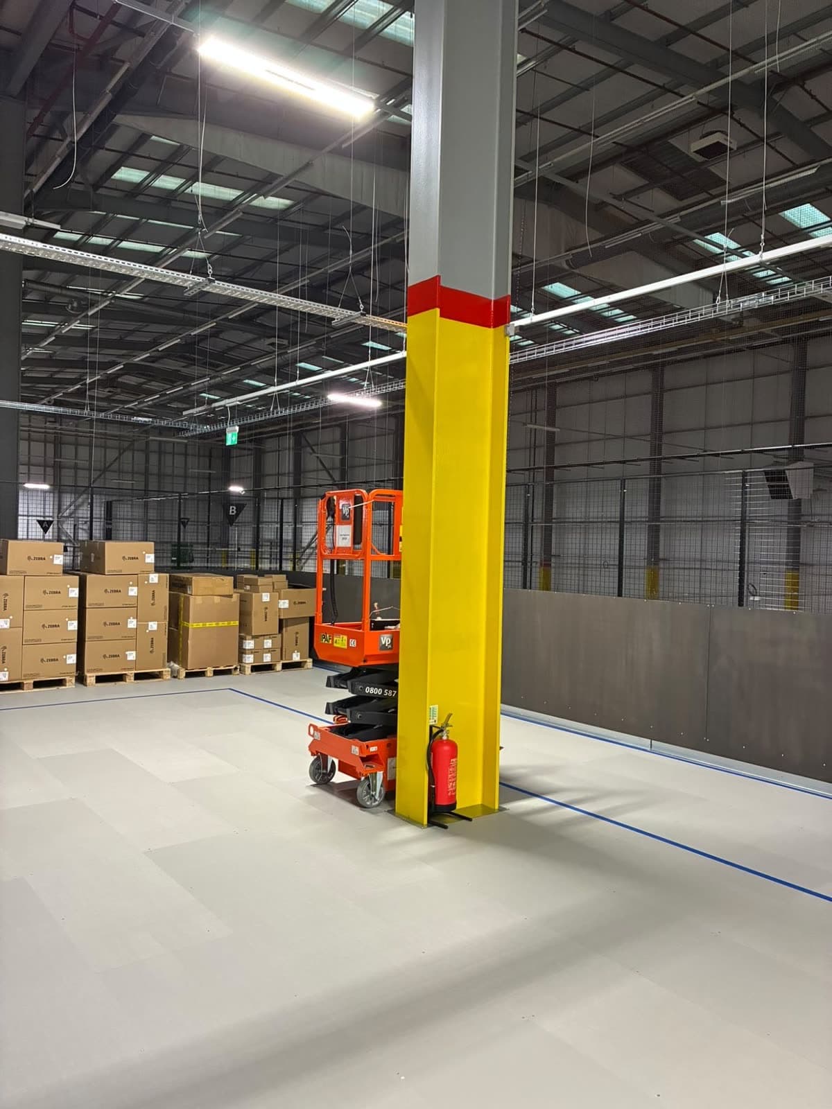 Column on the mezzanine deck, yellow with a red band near the top, beside an orange access lift and a fire extinguisher