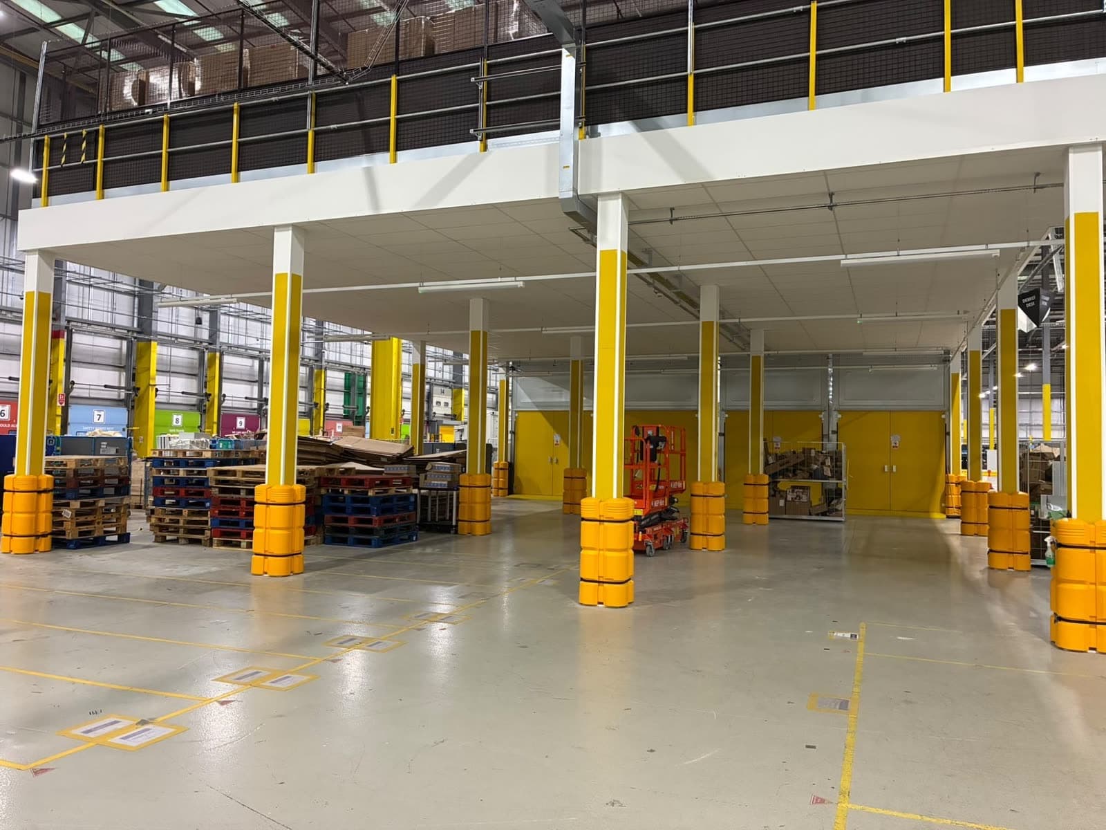 Columns under the new mezzanine at Amazon Lutterworth, painted yellow with a white band at the top, with an orange access lift between them